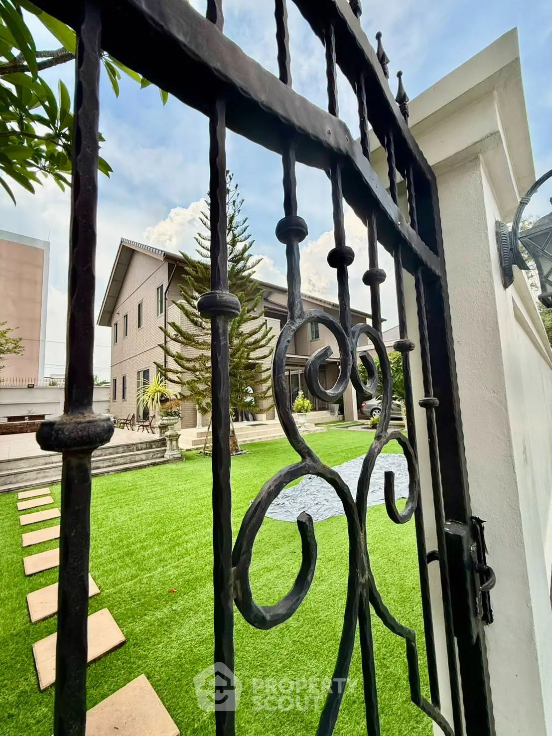 Charming gated entrance to a spacious garden with a modern house in the background.
