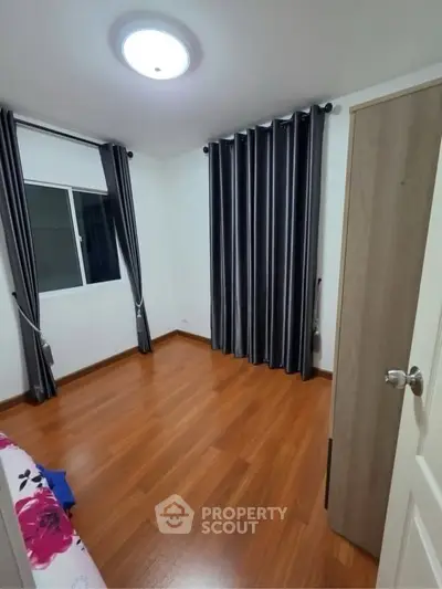 Spacious bedroom with wooden flooring and elegant curtains in modern apartment.