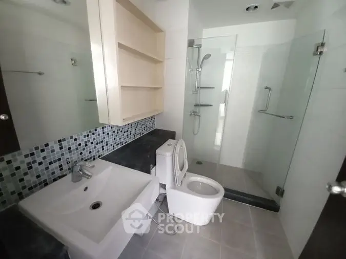 Modern bathroom with sleek design, featuring a glass shower enclosure, stylish tiling, and a well-lit vanity area for a refreshing ambiance.