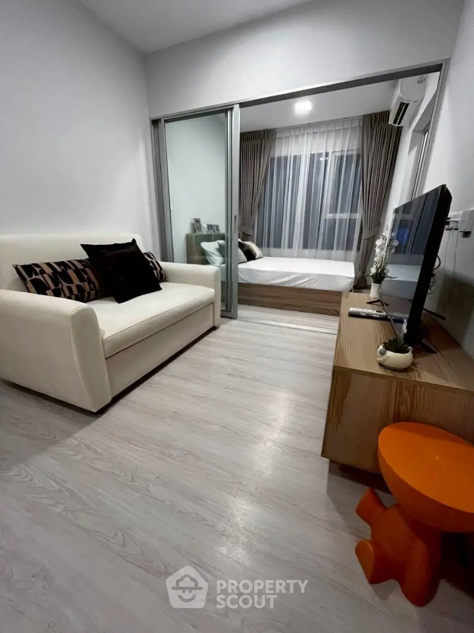 Modern living room with cozy sofa and TV, leading to a stylish bedroom with glass sliding doors.