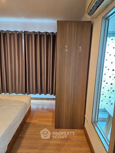 Cozy bedroom with wooden flooring and large window for natural light