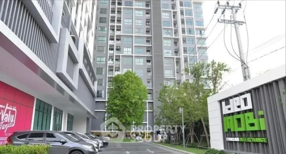 Modern high-rise condominium with parking and lush greenery in urban setting.