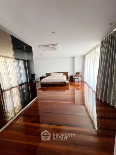 Spacious bedroom with polished wooden floors and large windows