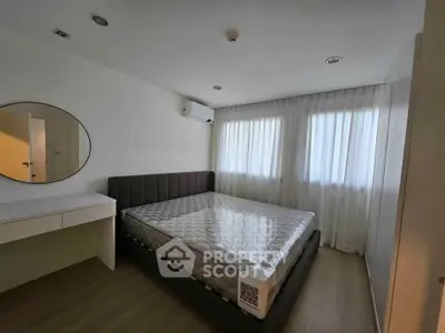 Modern bedroom with large bed, round mirror, and natural light from two windows.