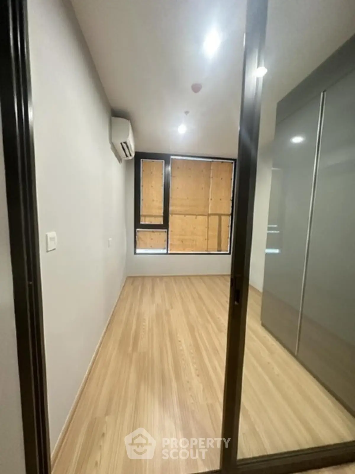 Spacious empty room with wooden flooring and large window, perfect for customization.