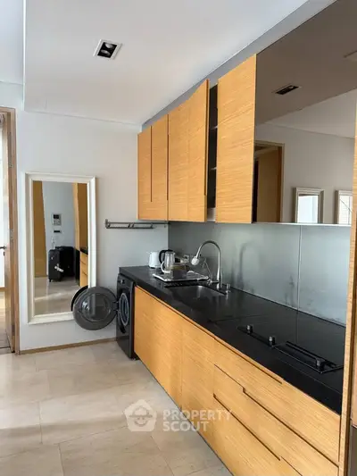 Modern kitchen with sleek wooden cabinets and built-in appliances, featuring a washing machine and stylish backsplash.