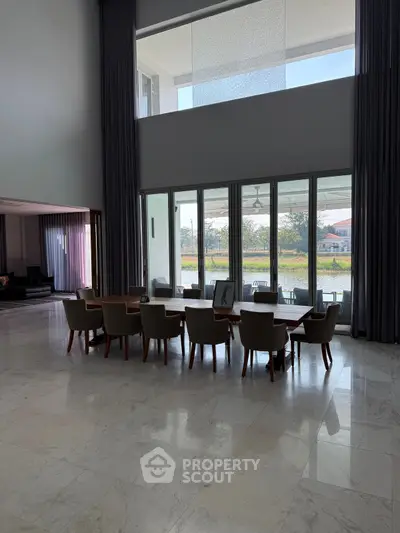 Luxurious modern dining area with high ceilings and large windows overlooking serene outdoor view.
