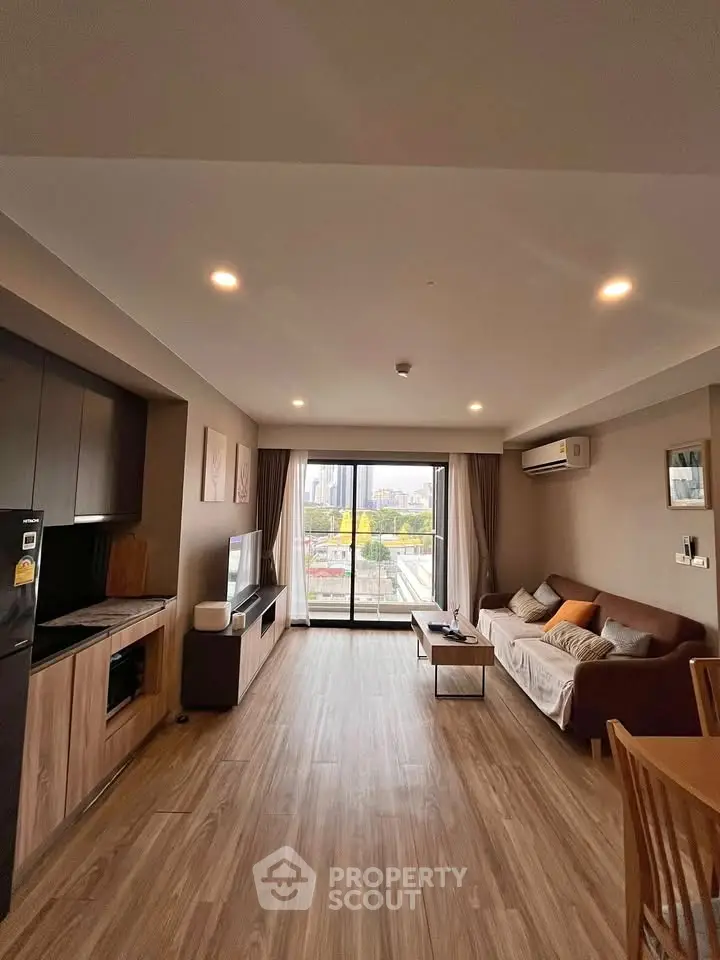 Spacious modern living room with large windows and city view, featuring stylish furniture and wooden flooring.