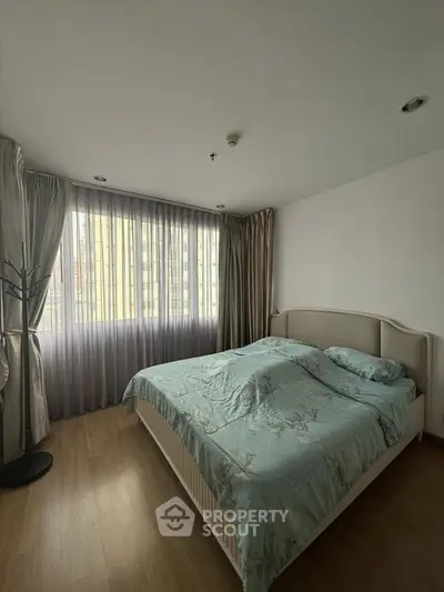 Spacious bedroom with large window and elegant curtains in modern apartment.