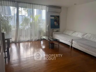 Spacious living room with hardwood floors and large windows offering city views.