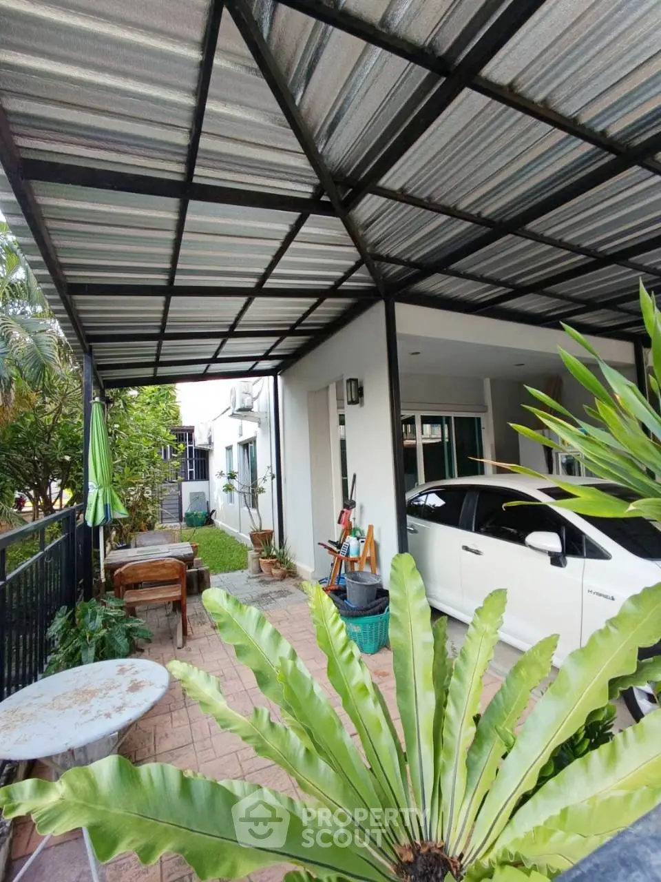 Charming covered carport with lush greenery and outdoor seating area in a modern home.