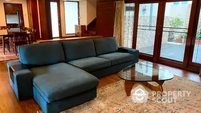 Spacious living room with modern sofa and glass coffee table, featuring large windows and wooden flooring.