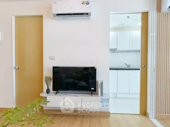 Modern living room with TV and air conditioning, open view to sleek kitchen.