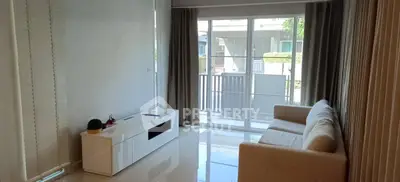 Bright living room with modern sofa and sleek TV cabinet, large windows open to a serene balcony view.