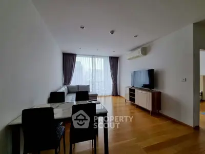 Spacious modern living room with wooden flooring and large window offering city views.