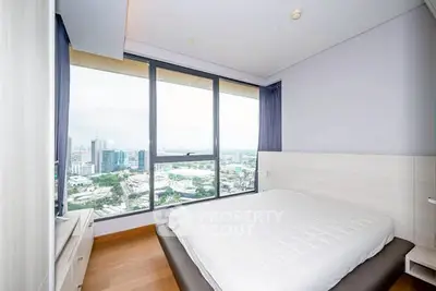 Modern bedroom with stunning city view through large windows, featuring minimalist decor and wooden flooring.