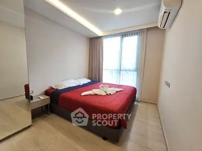 Modern bedroom with cozy red bedding and large mirror reflecting natural light from window.