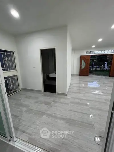Spacious modern living area with sleek flooring and open layout, featuring elegant entrance doors.