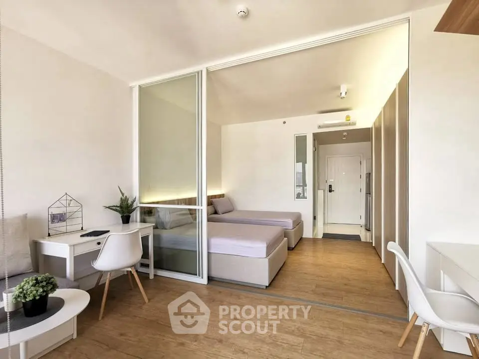 Modern studio apartment with twin beds and workspace, featuring sleek design and natural light.