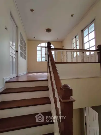 Elegant staircase with wooden railing and natural light in a spacious home interior.