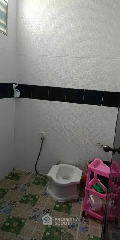 Compact bathroom with tiled walls and floor, featuring a squat toilet and storage shelf.