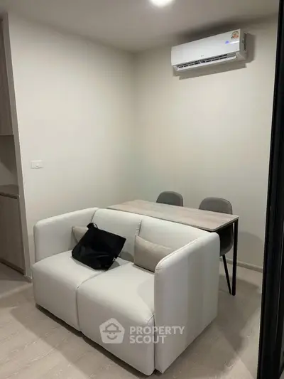 Cozy modern living area with compact sofa and dining table under air conditioning unit.