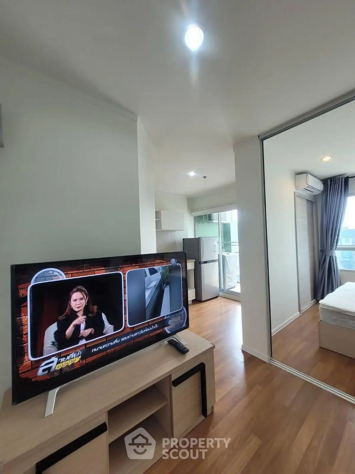 Modern apartment interior with TV, wooden flooring, and balcony view.