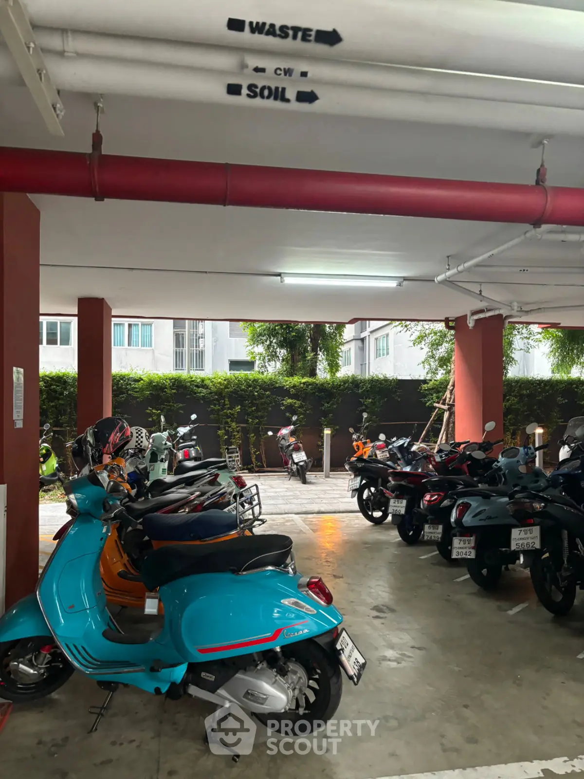 Covered parking area with multiple scooters and motorcycles in a residential building.