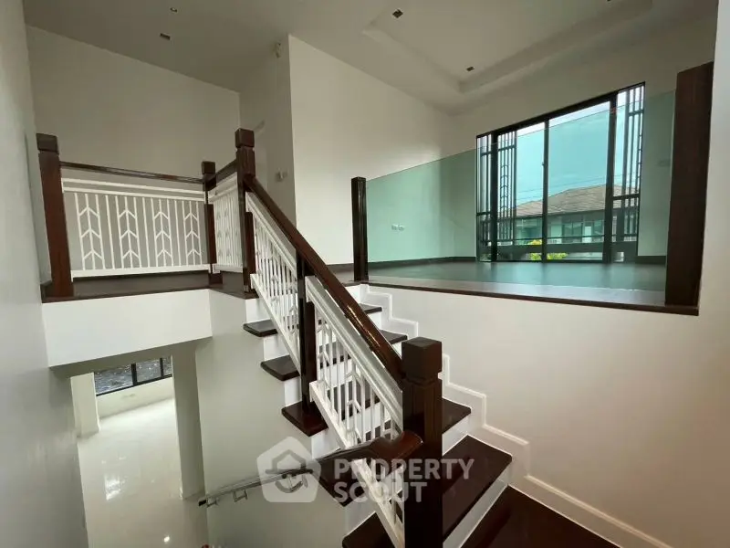Elegant modern staircase with wooden accents and glass railing in a spacious home interior.