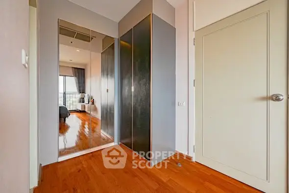 Modern apartment hallway with wooden flooring and mirrored closet doors.