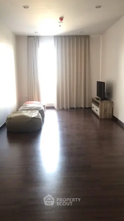 Spacious minimalist living room with bean bags and TV, featuring dark wood flooring.