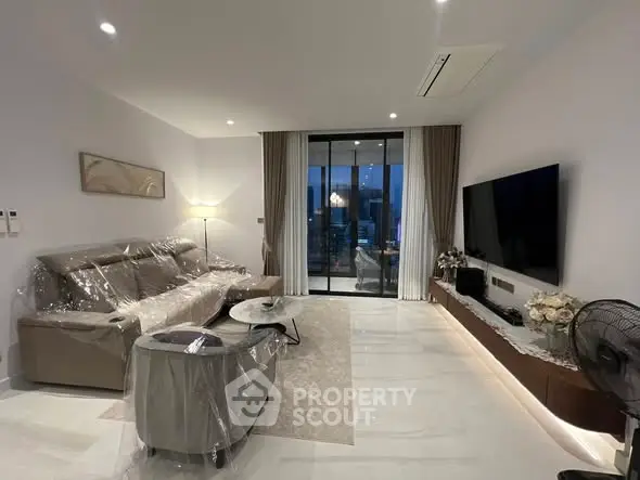 Modern living room with sleek furniture and large glass doors leading to a balcony with city views.