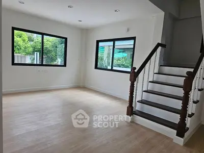 Spacious empty room with wooden staircase and large windows offering garden views.