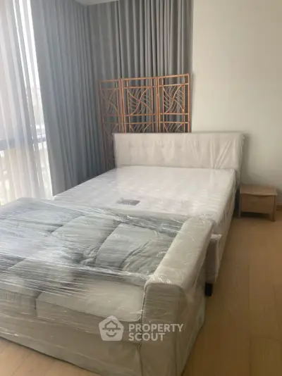 Spacious bedroom with modern decor and natural light, featuring a bed and sofa wrapped for protection.