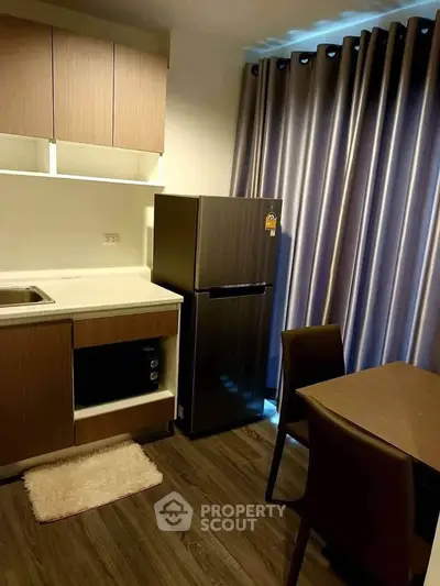 Modern kitchen with sleek cabinetry, compact fridge, and dining area in cozy apartment setting.