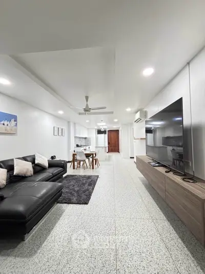 Spacious modern living room with sleek black leather sofa and large TV, open to dining area and kitchen.