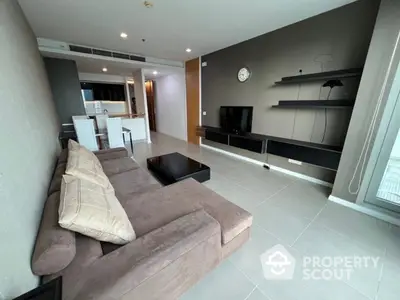 Spacious modern living room seamlessly connected to a sleek kitchen, featuring plush sofa, glossy tiles, and ample natural light.