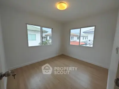 Bright empty bedroom with wooden flooring and large windows in modern home.