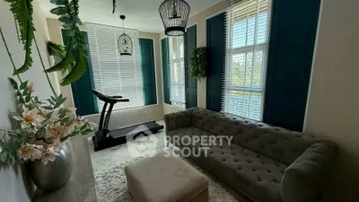 Charming living room with treadmill, elegant sofa, and large windows with shutters.
