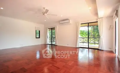 Spacious living room with hardwood floors and large windows overlooking greenery.