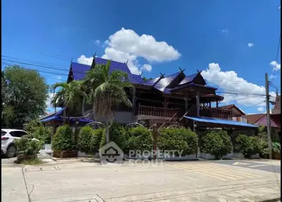 Charming traditional-style home with blue roof and lush greenery under a bright sky.
