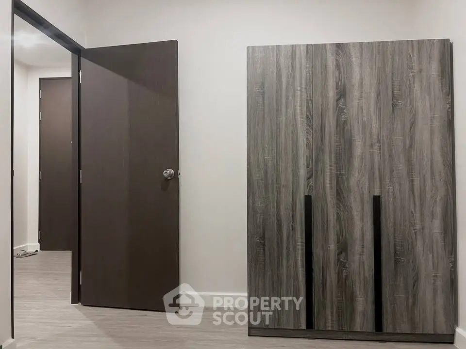 Modern interior with sleek wooden wardrobe and open door in a minimalist room.