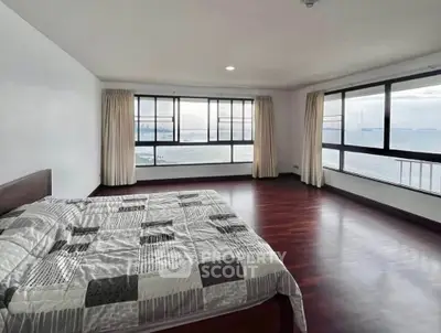 Spacious bedroom with stunning ocean view and large windows, featuring elegant wooden flooring.