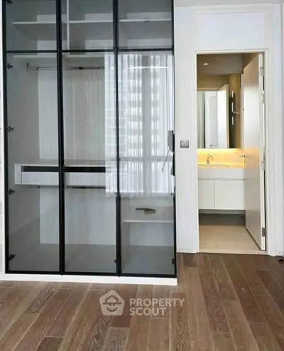 Modern apartment with glass closet and ensuite bathroom, featuring sleek design and wooden flooring.