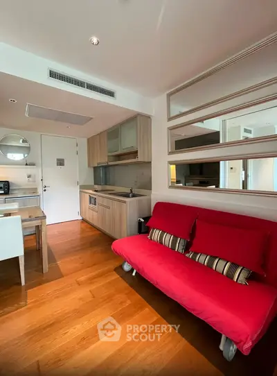 Modern living room with red sofa and open kitchen layout, featuring wooden flooring and stylish mirrors.