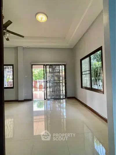 Spacious living room with large windows and polished tile flooring, offering natural light and garden views.