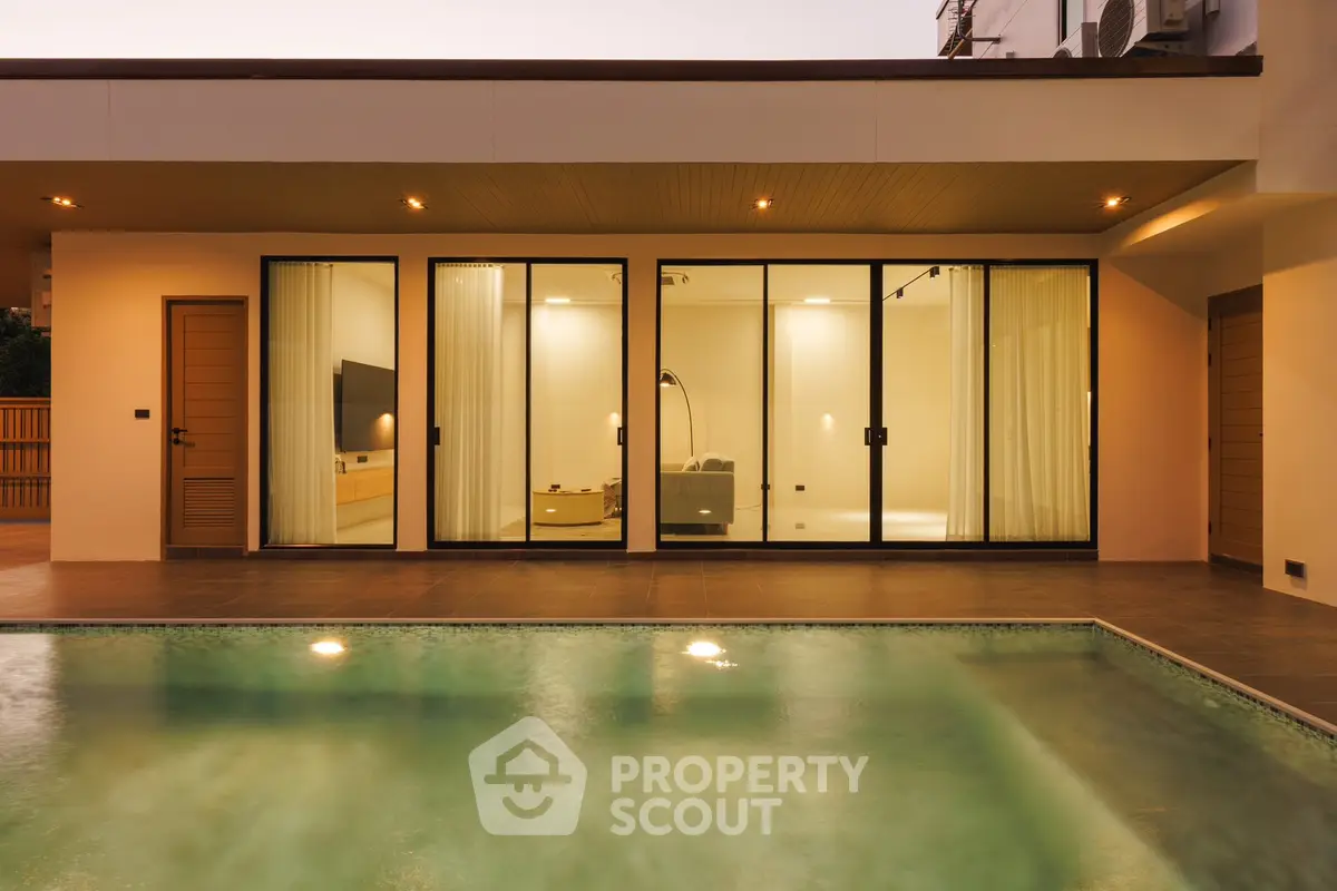 Luxurious modern home with illuminated pool and elegant glass facade at dusk.