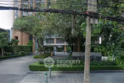 Modern residential building entrance with lush greenery and paved driveway in urban setting.