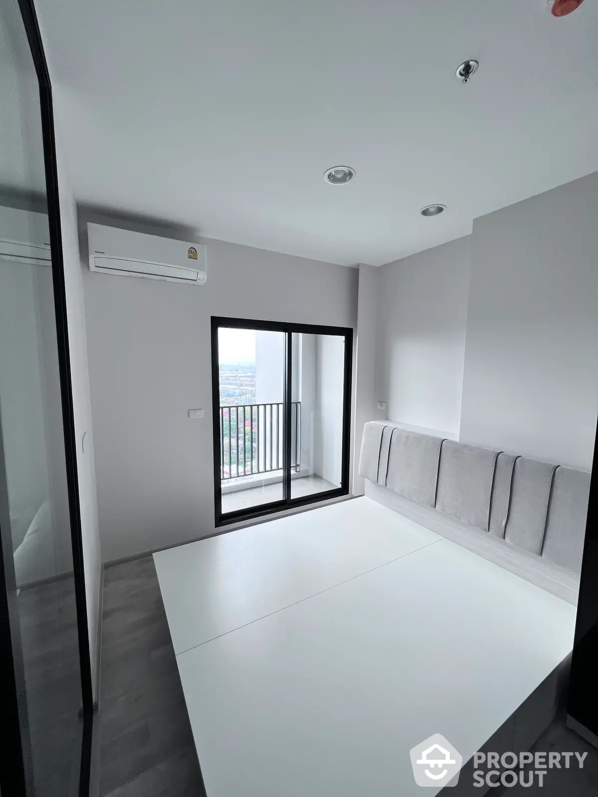 Modern minimalist living room with clean lines, ample natural light, and a comfortable built-in sofa, opening to a balcony with a view.