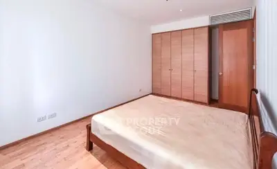 Spacious bedroom with wooden flooring and built-in wardrobe in modern apartment.